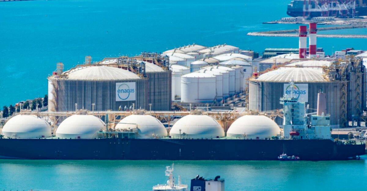 Aerial shot of a gas terminal featuring LNG storage tanks and tanker ships in turquoise waters