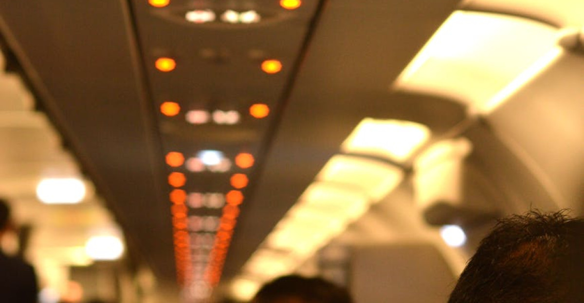 Interior of a well-lit airplane cabin showing the overhead safety signs and passenger seating