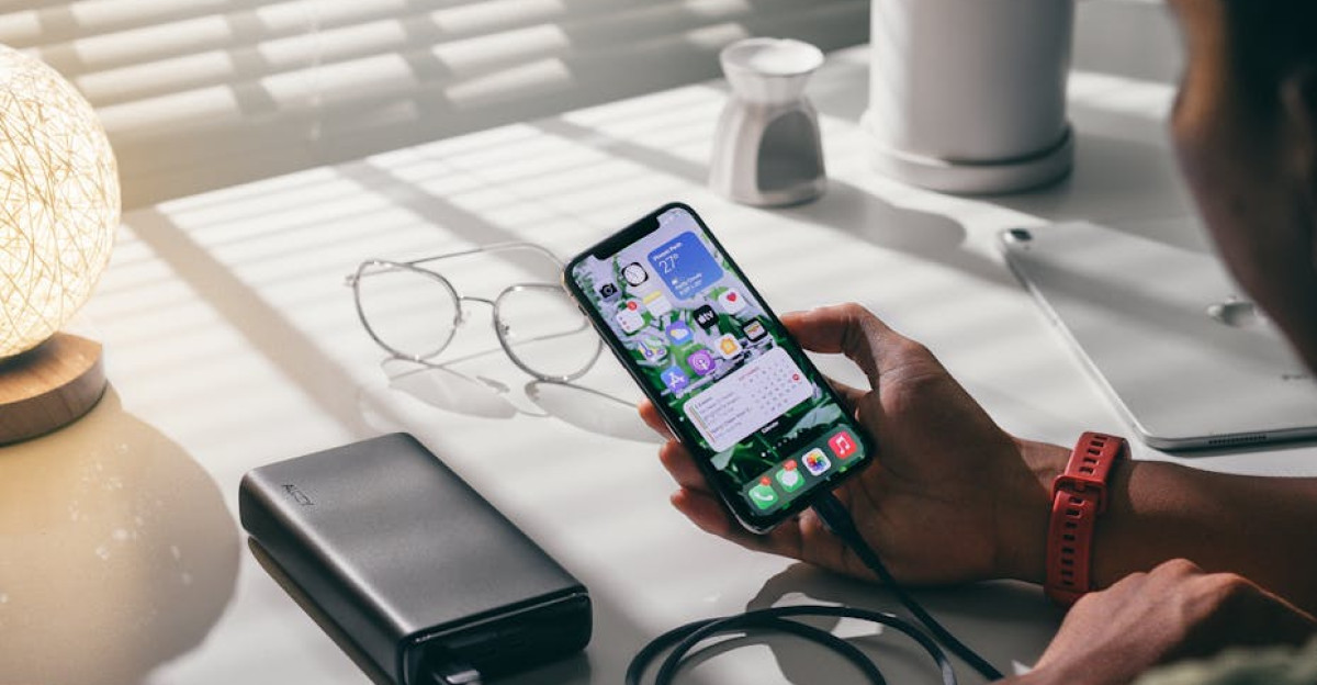 Person holding a smartphone connected to a power bank on a desk indoors showcasing modern technology