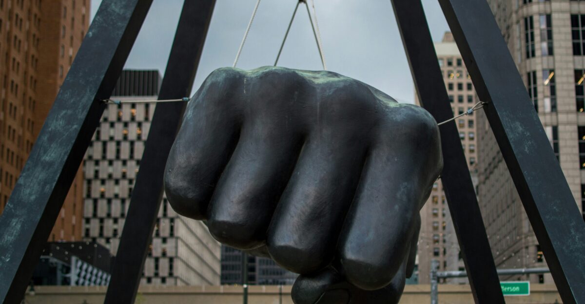 a statue of a fist is suspended by a crane