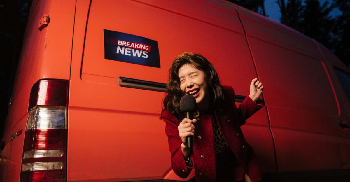 Asian woman reporter energetically broadcasting with a microphone in front of a news van at night