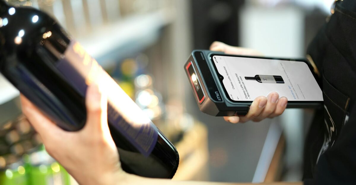 Close-up of a person scanning a wine bottle with a portable scanner in a store