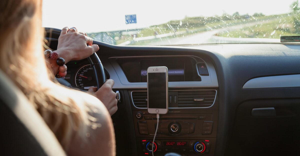 View from behind a woman driving a car on a sunny day with a phone mounted on the dashboard