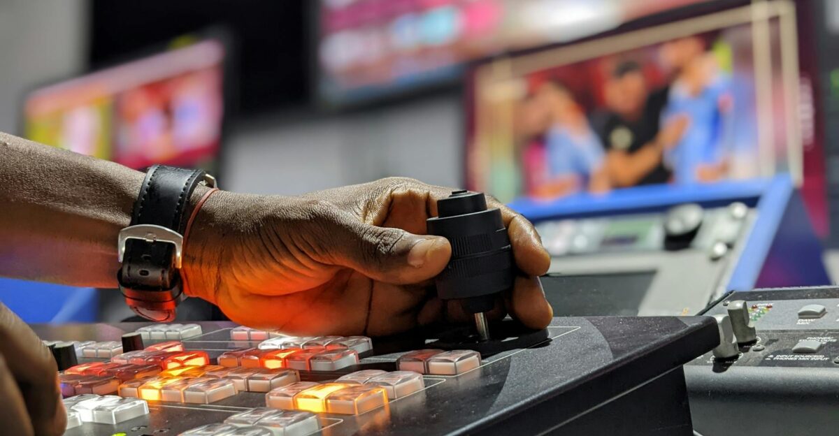 A hand operates a broadcast control mixer in a television studio setting