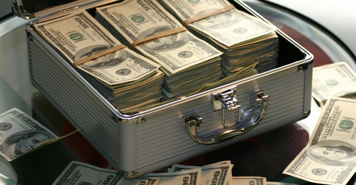Open briefcase filled with stacks of hundred dollar bills on a glass table representing wealth