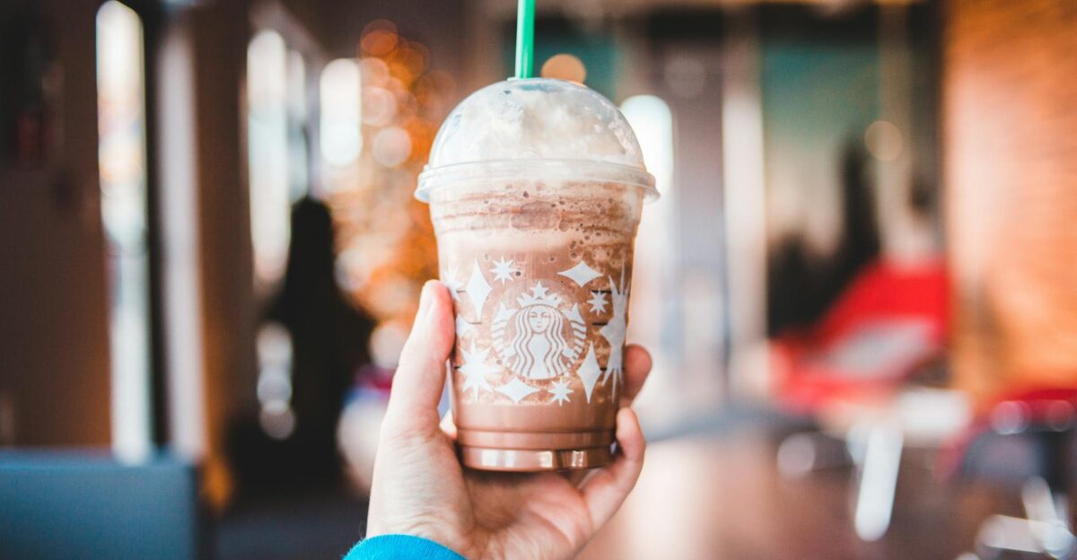 Close-up of a hand holding a cold Starbucks coffee drink indoors with blurred background