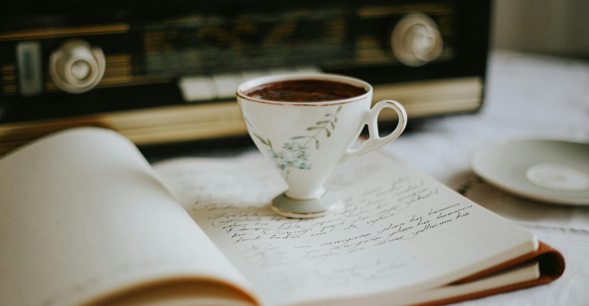 A vintage teacup on an open notebook with an old radio in the background creating a nostalgic atmosphere