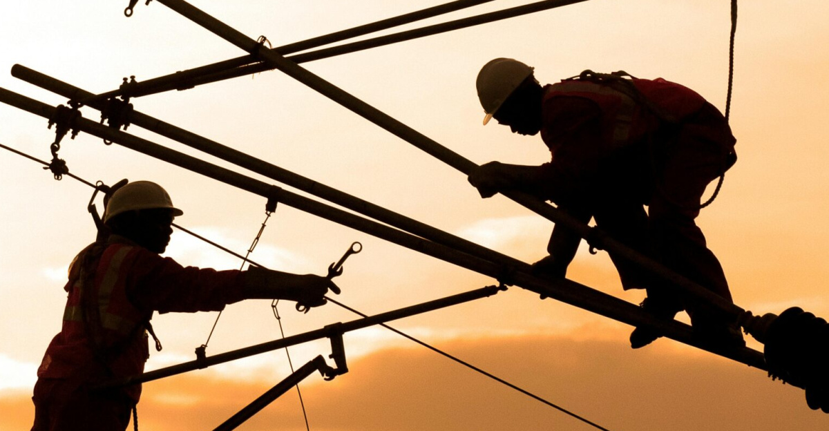 Electricians repairing power lines at sunset, showcasing teamwork and safety.
