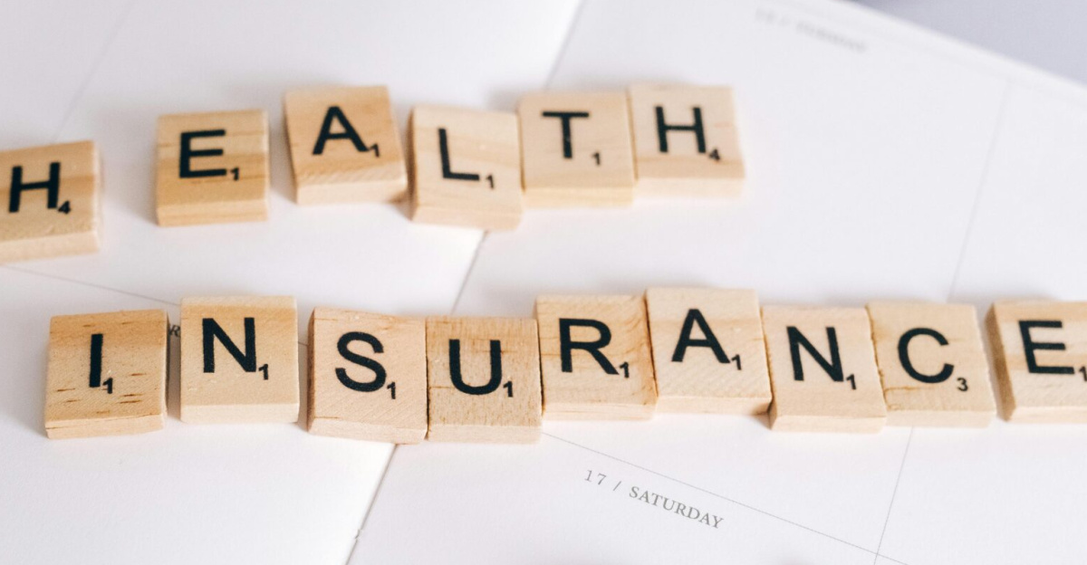 Scrabble tiles spelling 'Health Insurance' on planner with pills and laptop, symbolizing healthcare planning.